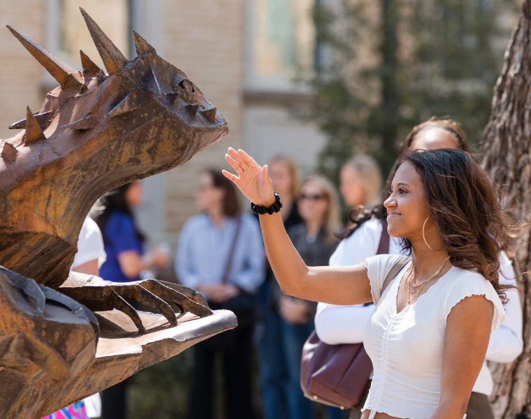Girl putting her hand out to rub the nose on horned frog statue